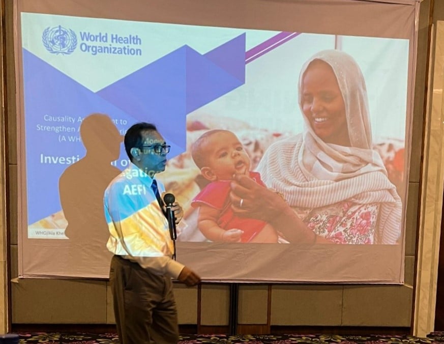A male doing a presentation while standing in front of projector screen.